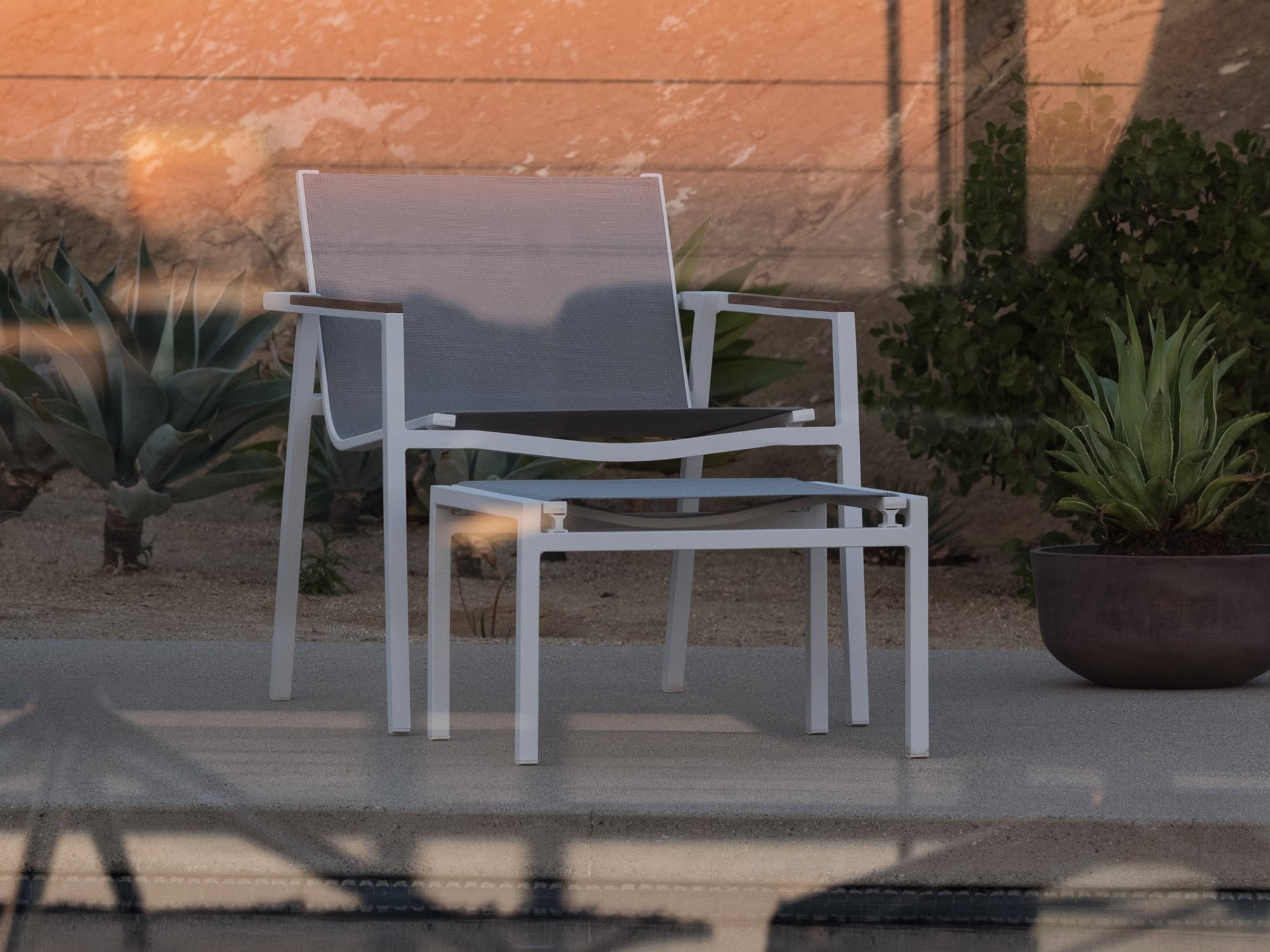 White and teak outdoor lounge chair with matching ottoman on pool deck